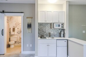 A modern kitchen with white cabinets, a microwave, and a herringbone tile backsplash.