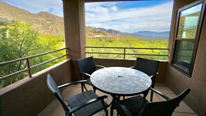 Un balcon avec une table ronde et quatre chaises, donnant sur un paysage montagneux.