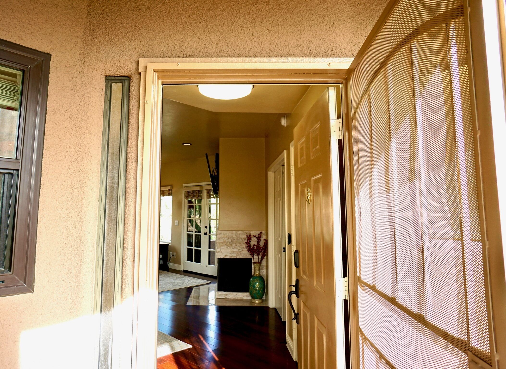 A hallway with a wooden floor, a door with a metal screen, and a window with blinds.