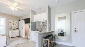 A modern kitchen with white cabinetry, a brick backsplash, and a small island with stools. - Pretty Peony Steps to Pool - Myrtle Beach, SC (Myrtle Beach)