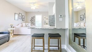 A modern living room with a sofa, a coffee table, and two bar stools. There is a large mirror on the wall and a ceiling fan. - Pretty Peony Steps to Pool - Myrtle Beach, SC (Myrtle Beach)