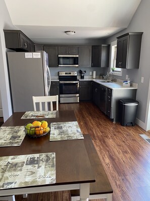 A modern kitchen with dark cabinetry, stainless steel appliances, and a dining table set with placemats and a fruit bowl.