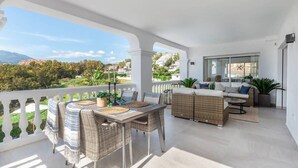 A balcony with a dining area, wicker furniture, and a view of a green landscape. - Villa Alva | Luxe Heated Pool Cinema Sunset Views (Marbella)