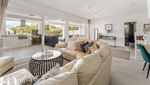 A spacious living room with a beige sofa, a coffee table, and a view of the outdoors. - Villa Alva | Luxe Heated Pool Cinema Sunset Views (Marbella)