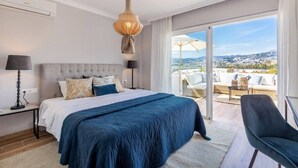 A bedroom with a large bed, a view of the city, and a balcony with outdoor furniture. - Villa Alva | Luxe Heated Pool Cinema Sunset Views (Marbella)