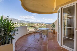 Ein Balkon mit Tisch und Stühlen, einem Blumentopf und Blick auf eine Berglandschaft.