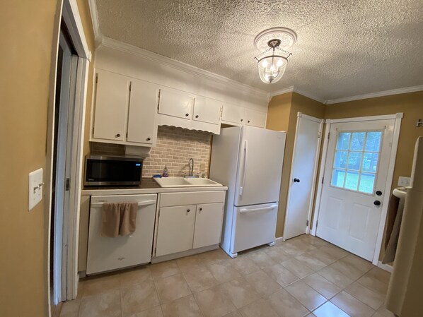 A kitchen with white cabinets, a microwave, a sink, and a refrigerator.