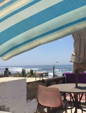 Un patio frente a la playa con sombrillas a rayas, una mesa y sillas.
