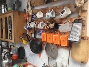 A kitchen with various utensils and cookware hanging on the wall, a wooden cabinet, and a grater on the counter.