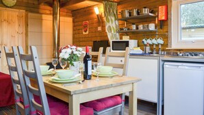 A cozy wooden cabin with a dining table set for two, a microwave, and a small refrigerator. - 1 bedroom accommodation in Brocklebank, near Caldbeck and Uldale (Brocklebank, near Caldbeck and Uldale)