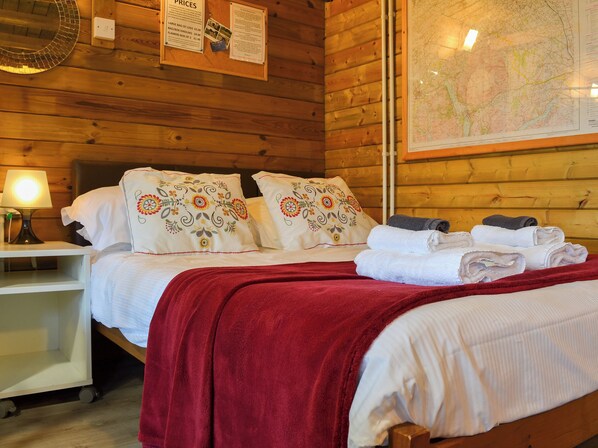 Una camera in una baita di legno con un letto, cuscini, una mappa e un comodino.