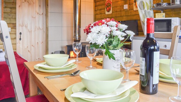 A wooden interior with a dining table set for two, featuring green plates, bowls, and a bottle of wine. - 1 bedroom accommodation in Brocklebank, near Caldbeck and Uldale (Brocklebank, near Caldbeck and Uldale)