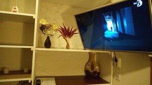 Una televisione appesa al muro, un vaso con fiori e un telecomando su un tavolo.