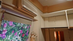Una stanza con condizionatore a soffitto, un blindo alla finestra con motivo floreale e una porta parzialmente visibile.