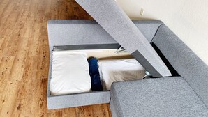 Un divano letto convertibile con materasso, un pavimento in legno e una parete bianca.