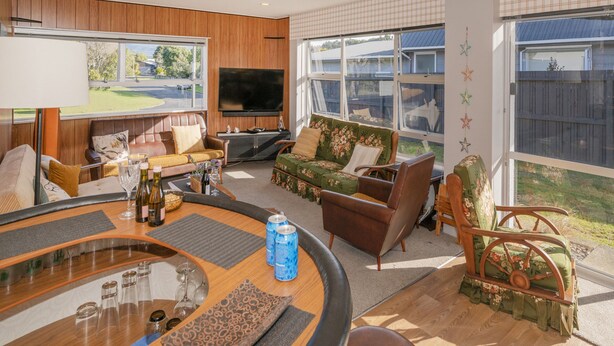 A modern living room with a large flat-screen TV, comfortable seating, and a view of the outdoors. - Lintons Sunshine Retreat - Whangamata Home (Whangamata)