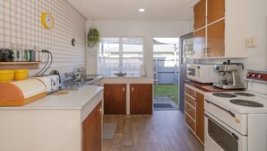 A kitchen with wooden cabinets, a microwave, a stove, and a sink. - Lintons Sunshine Retreat - Whangamata Home (Whangamata)
