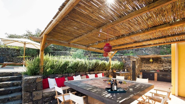 An outdoor dining area with a stone wall, wooden chairs, and a table set for two. - Villa for 10 People with private pool, garden and free WiFi (Randazzo)
