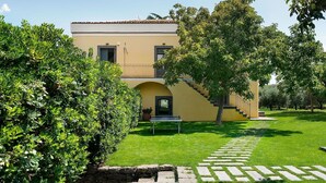A two-story building with a yellow facade, a stone staircase leading to the upper level, and a well-maintained lawn with a stone pathway. - Villa for 10 People with private pool, garden and free WiFi (Randazzo)