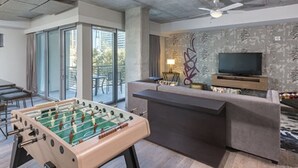 A modern living room with a foosball table, a sofa, a TV, and a balcony with glass doors. - Prime Austin 2 BR downtown new location (Austin)
