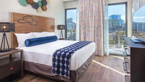 A modern hotel room with a large bed, a desk, and a view of the city through large windows. - Prime Austin 2 BR downtown new location (Austin)