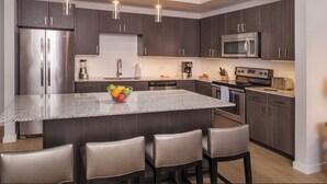 A modern kitchen with dark wood cabinets, stainless steel appliances, a granite island, and a seating area with leather chairs. - Prime Austin 2 BR downtown new location (Austin)