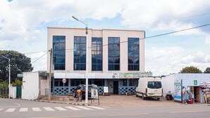 Un edificio con ventanas amplias, una fachada con letrero de cafetería y una furgoneta estacionada adelante.