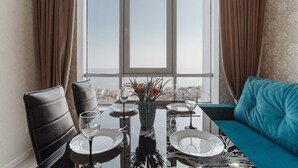 A dining area with a table set for two, a sofa, and a window with curtains. - Apartments Arcadia. Panorama of the sea. 3 bedrooms  (Odessa)
