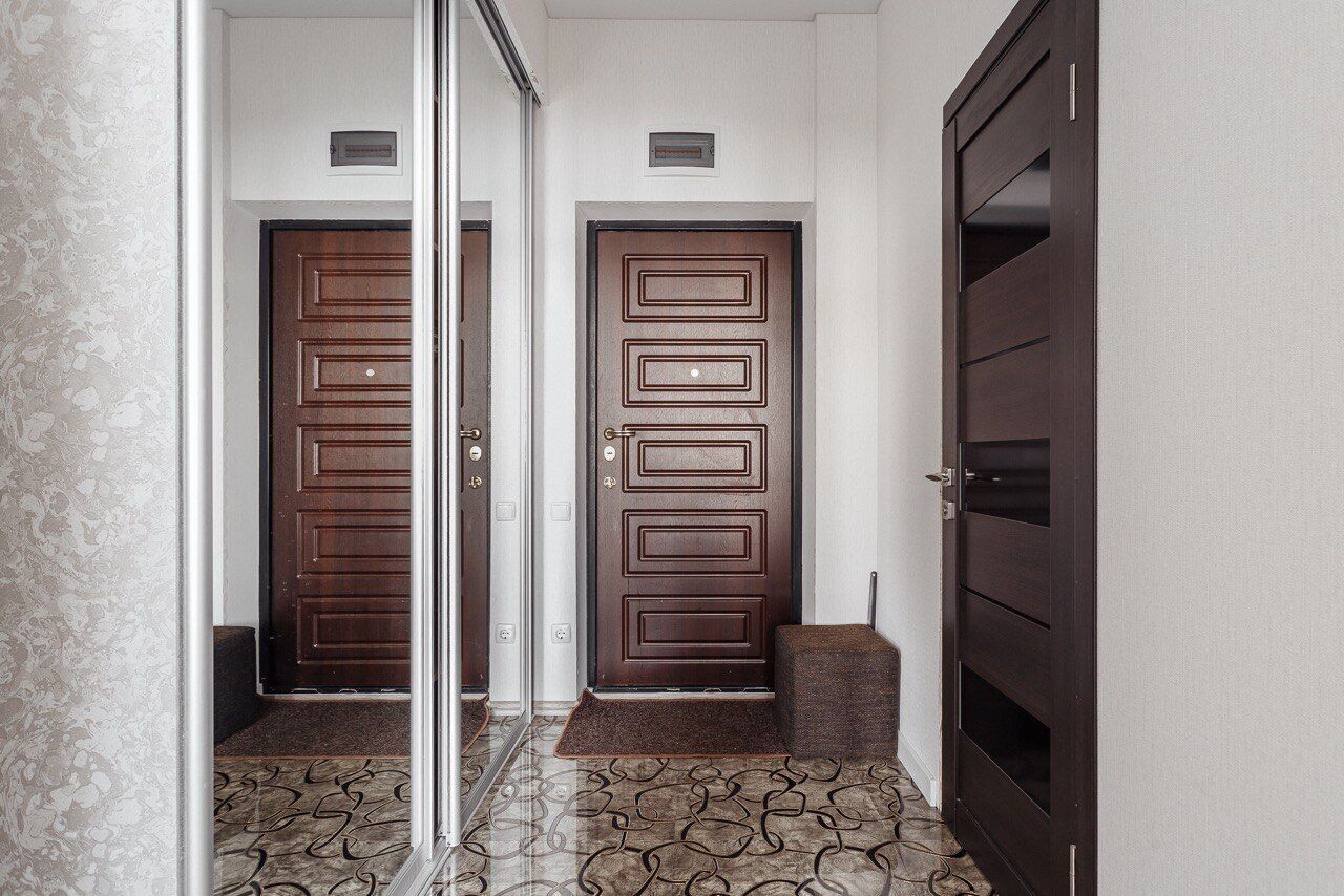 A hallway with two wooden doors, a patterned floor, and a bench.