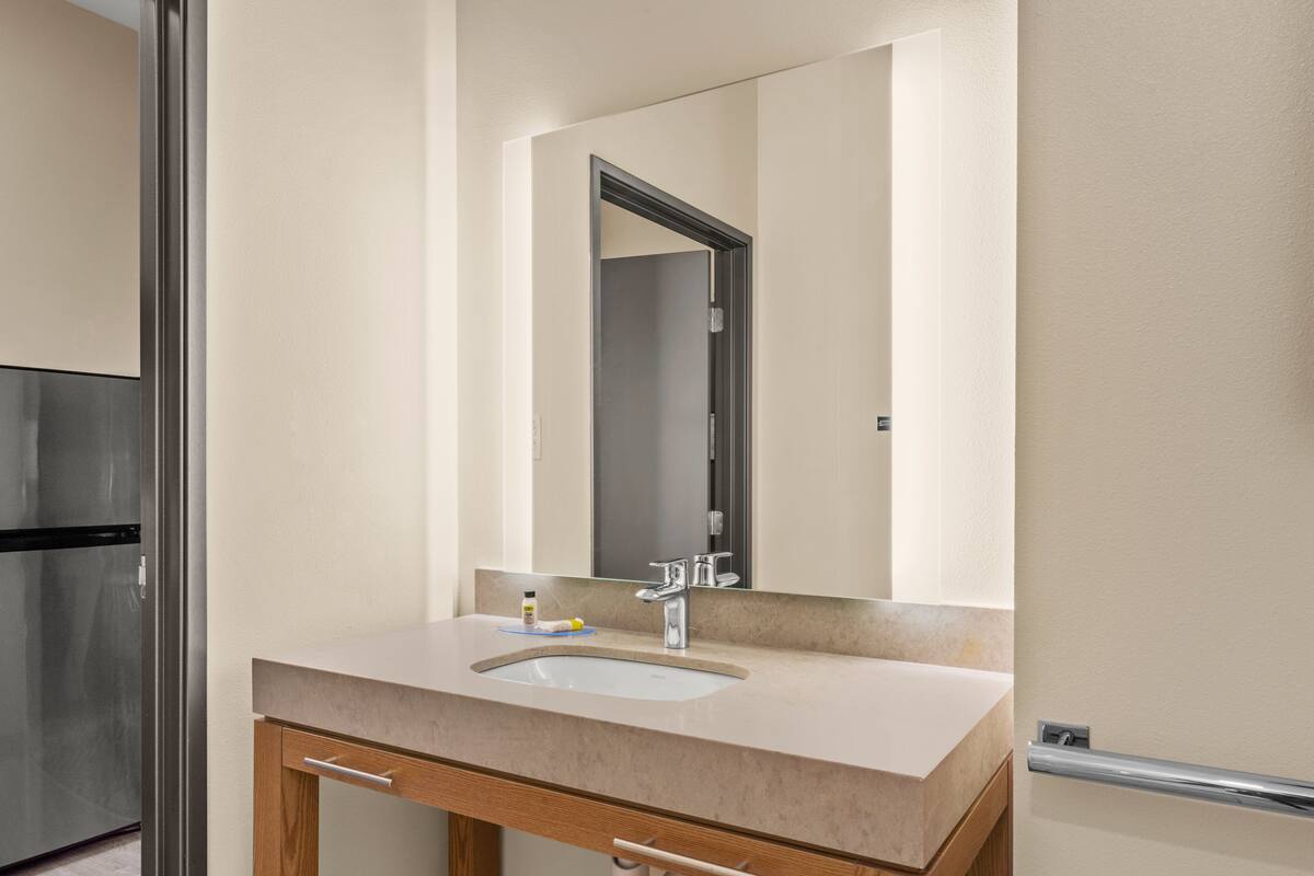 A bathroom with a sink, mirror, and a door leading to another room.