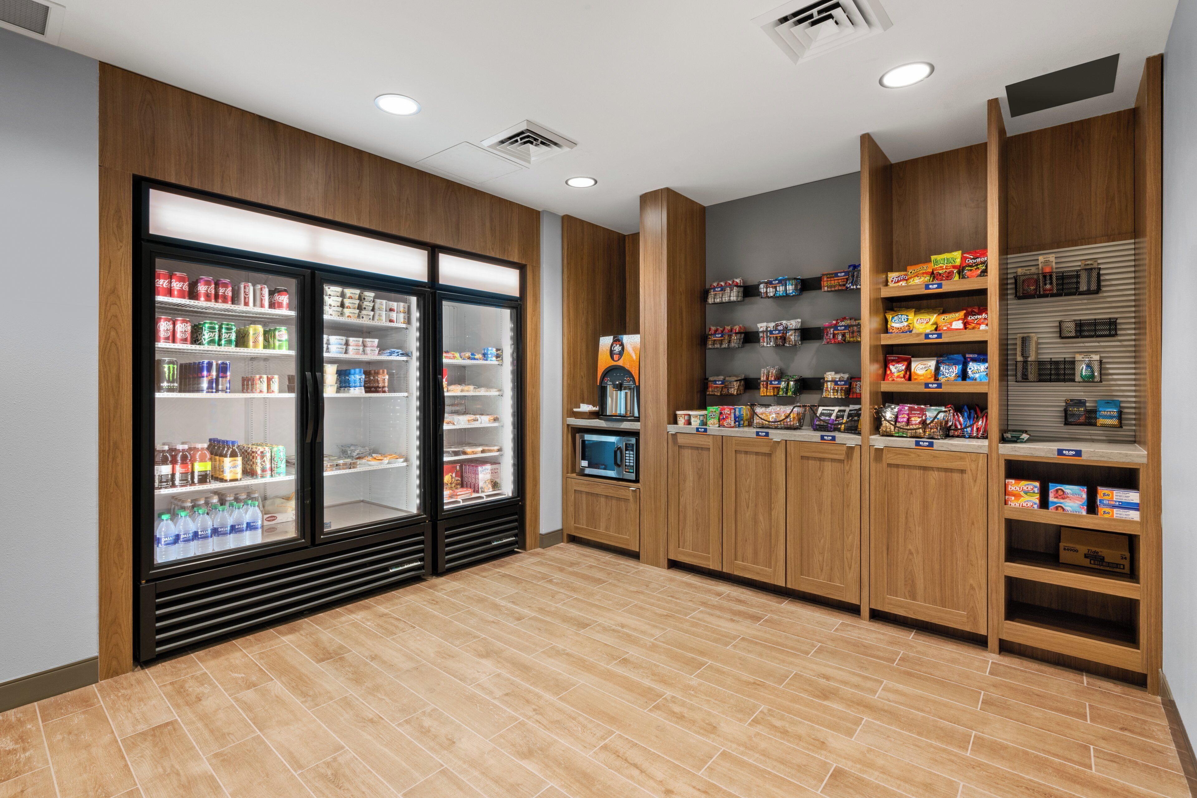 Una barra de aperitivos limpia y bien iluminada, con bebidas refrigeradas, una máquina de café y estantes repletos de snacks y bebidas.