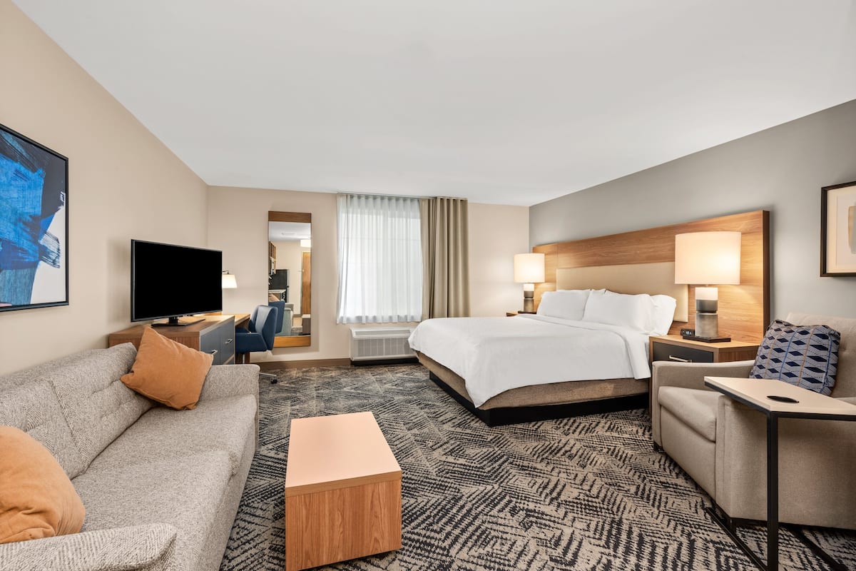 A hotel room with a bed, a sofa, a TV, a desk, and a window with curtains.