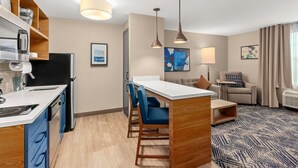 A modern hotel room with a kitchenette, a dining area with blue chairs, a sofa, and a patterned rug. - Candlewood Suites Sumner by IHG (Sumner)