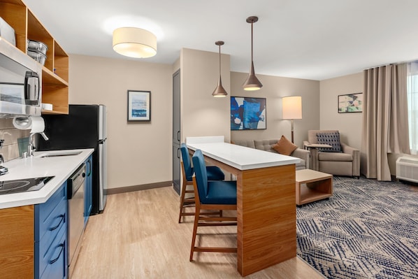 A modern hotel room with a kitchenette, a dining area with blue chairs, a sofa, and a patterned rug. - Candlewood Suites Sumner by IHG (Sumner)