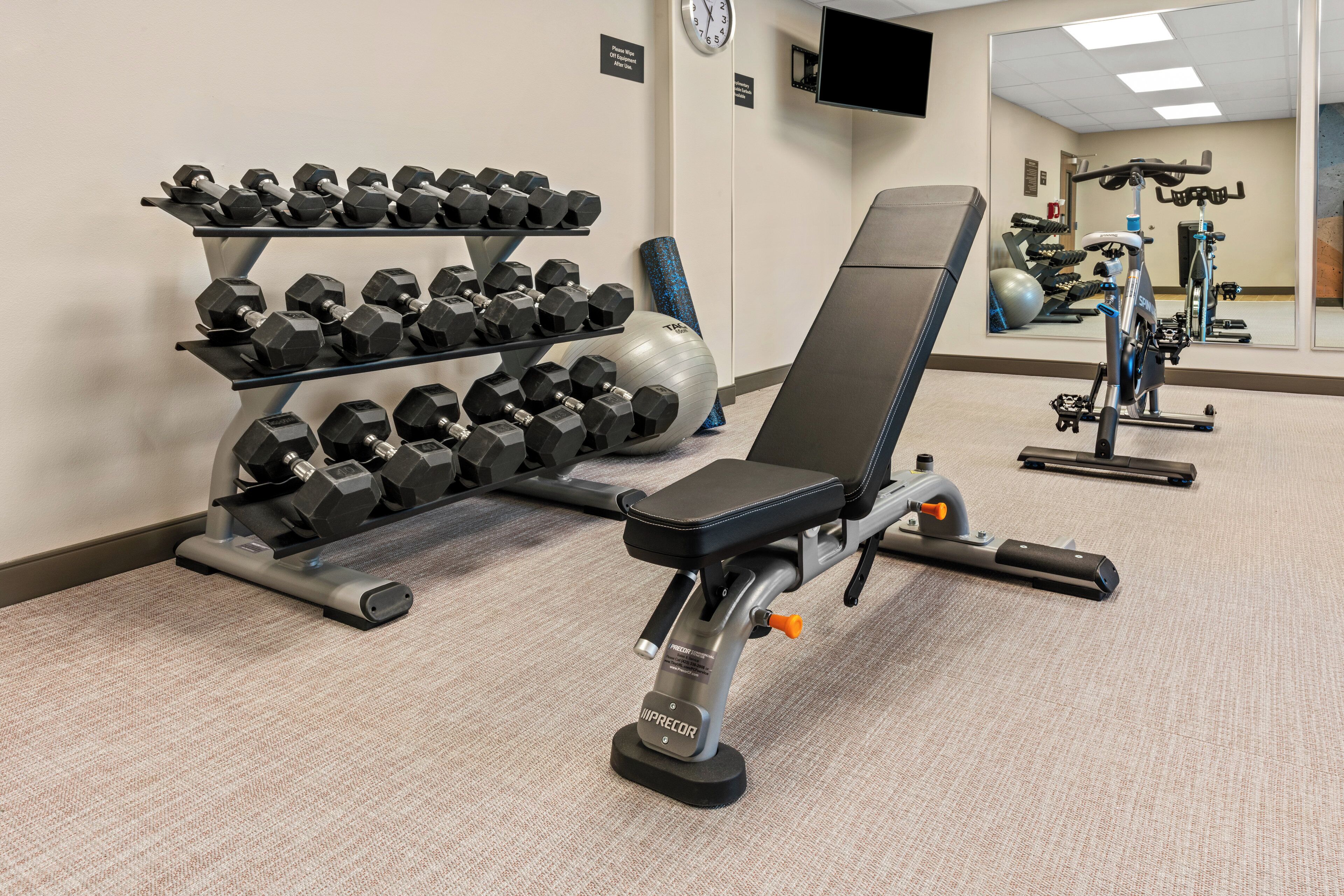 Une salle de sport équipée de matériel d’exercice, notamment des haltères, un banc et un vélo d’appartement.