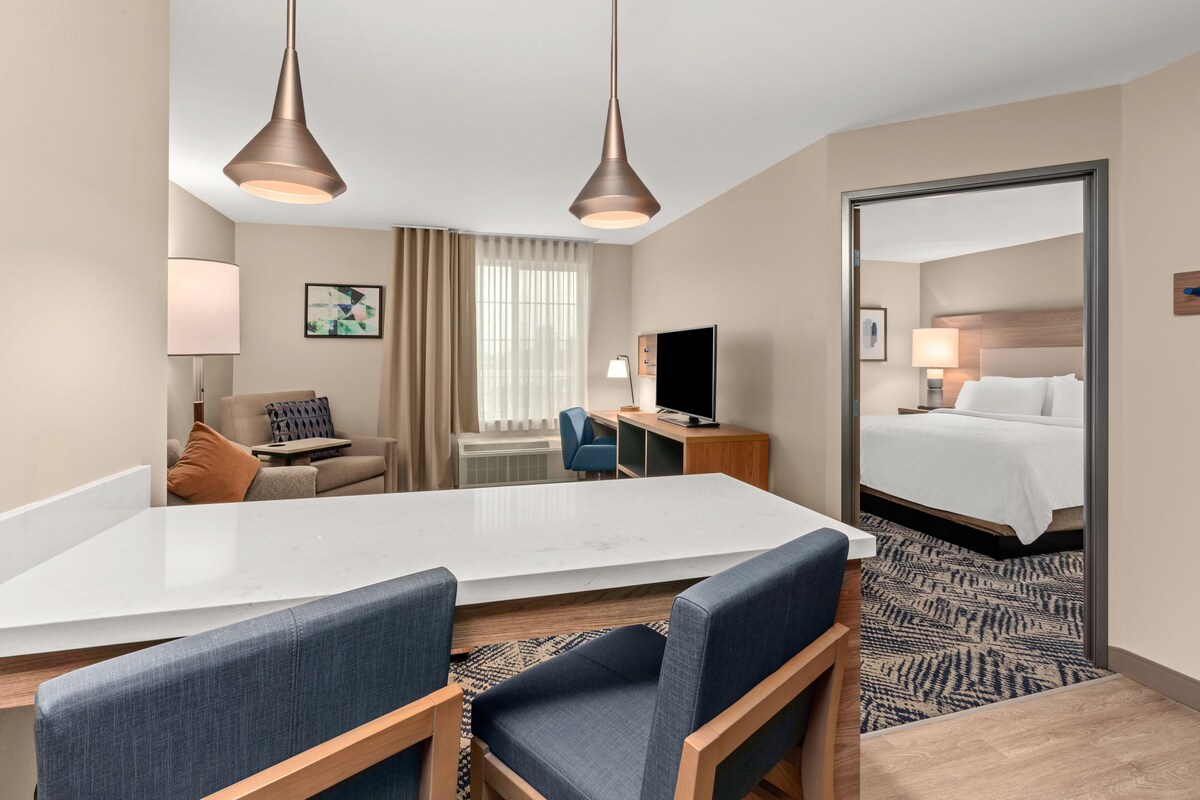 A hotel room with a large bed, a desk with a computer, a chair, a sofa, and two pendant lights.