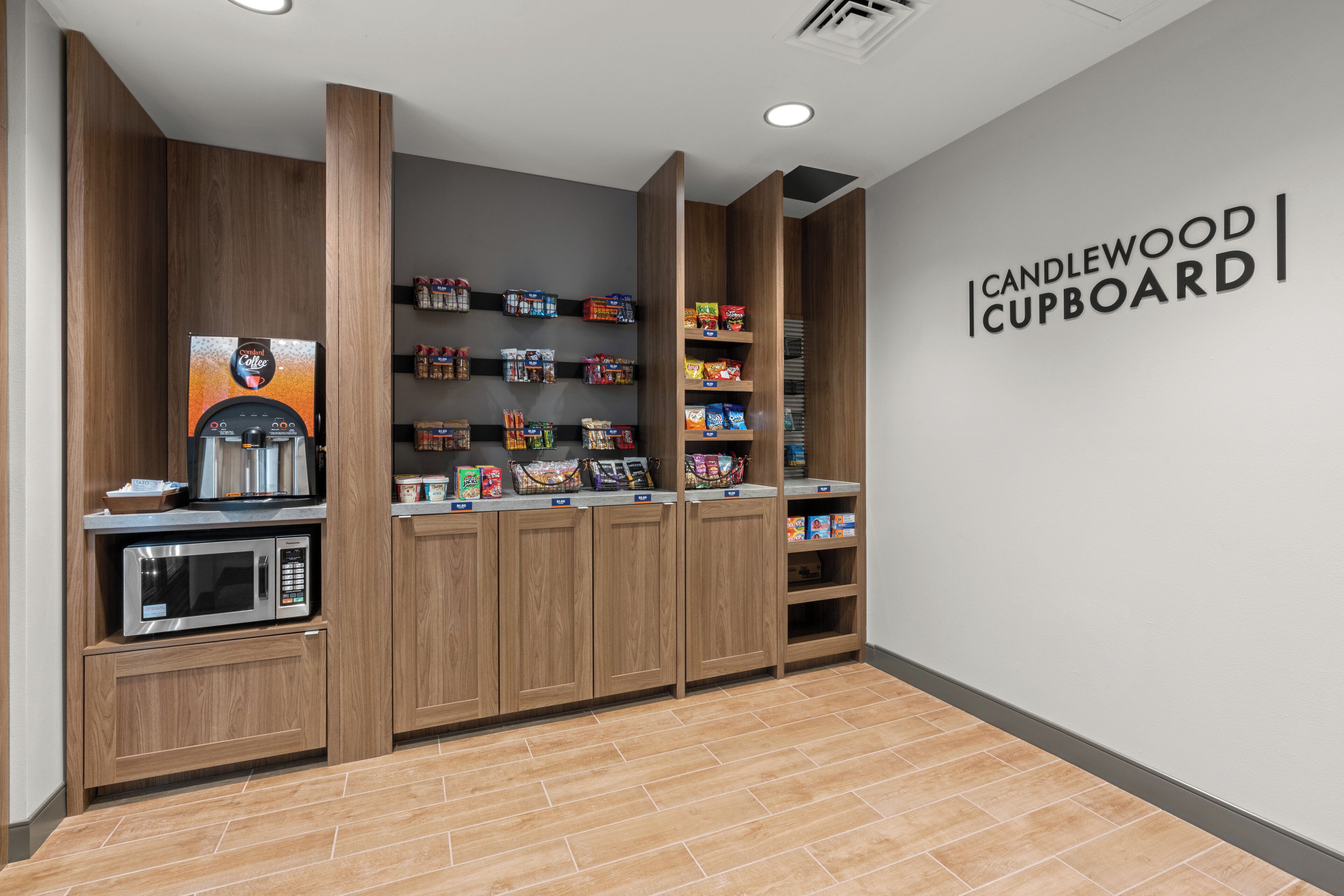 A kitchenette area with a coffee machine, shelves stocked with snacks, and a sign reading 'CANDLEWOOD CUPBOARD'.