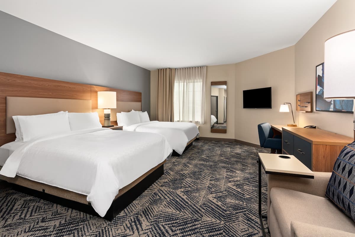A hotel room with two beds, a desk, a chair, a TV, and a mirror.