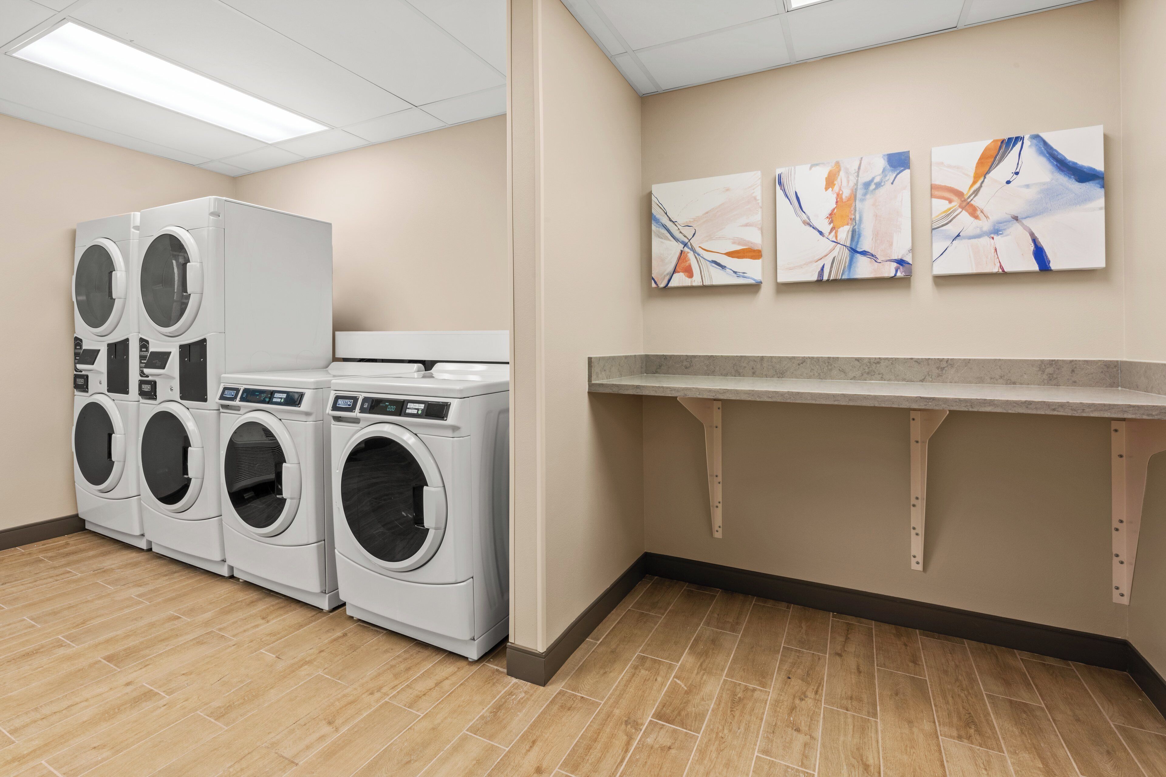 A laundry room with multiple washing machines, a countertop, and abstract wall art.