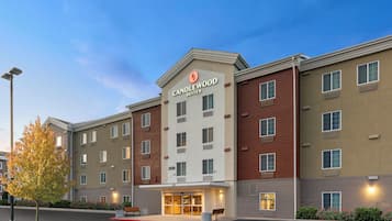 A multi-story hotel with a prominent 'Candlewood Suites' sign, a parking lot, and a landscaped area with benches.