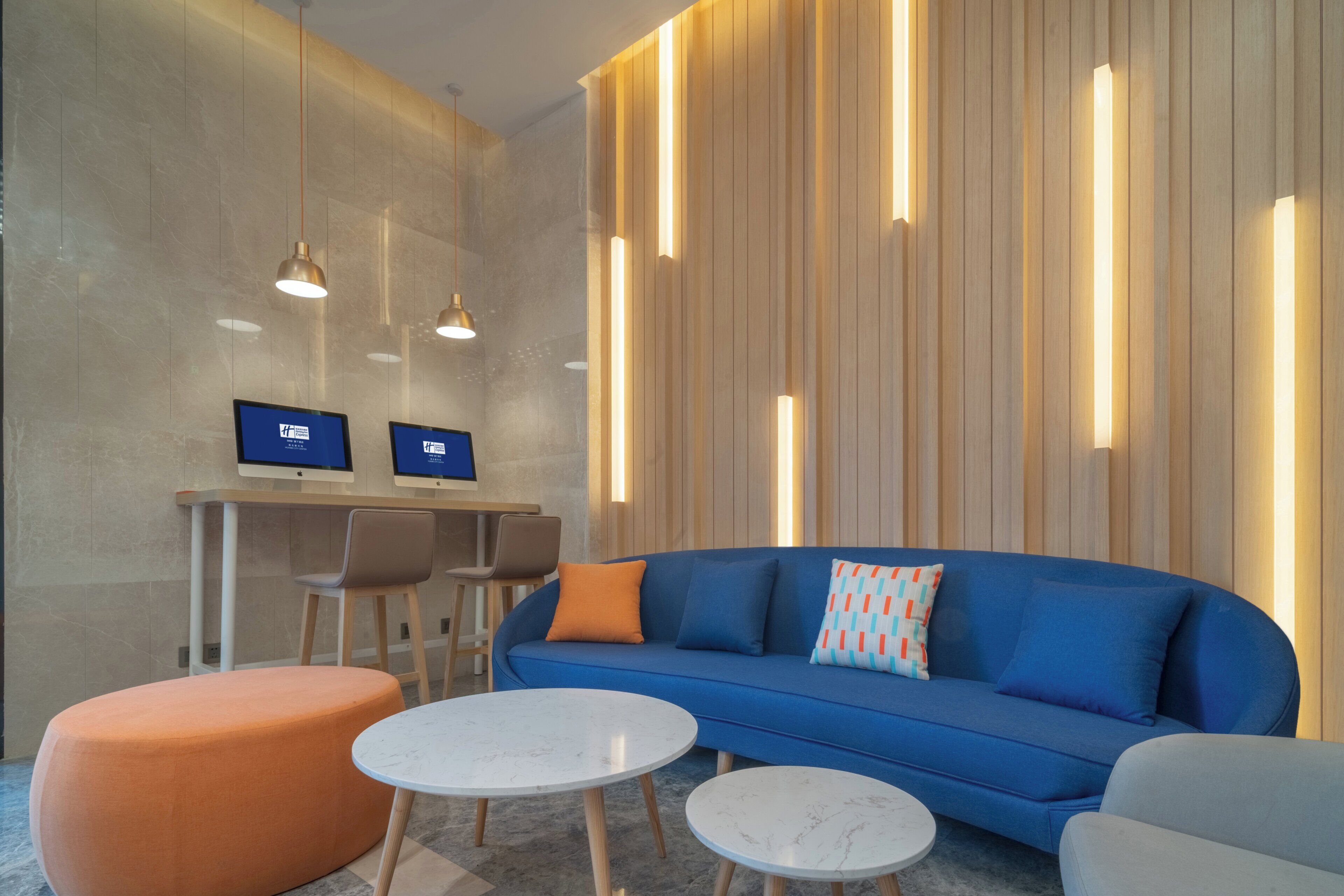 Una zona relax moderna con un divano blu, un poggiapiedi arancione e due tavolini in marmo bianco.