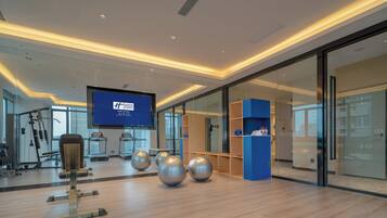 A modern fitness center with exercise equipment, a large screen displaying information, and a glass partition.