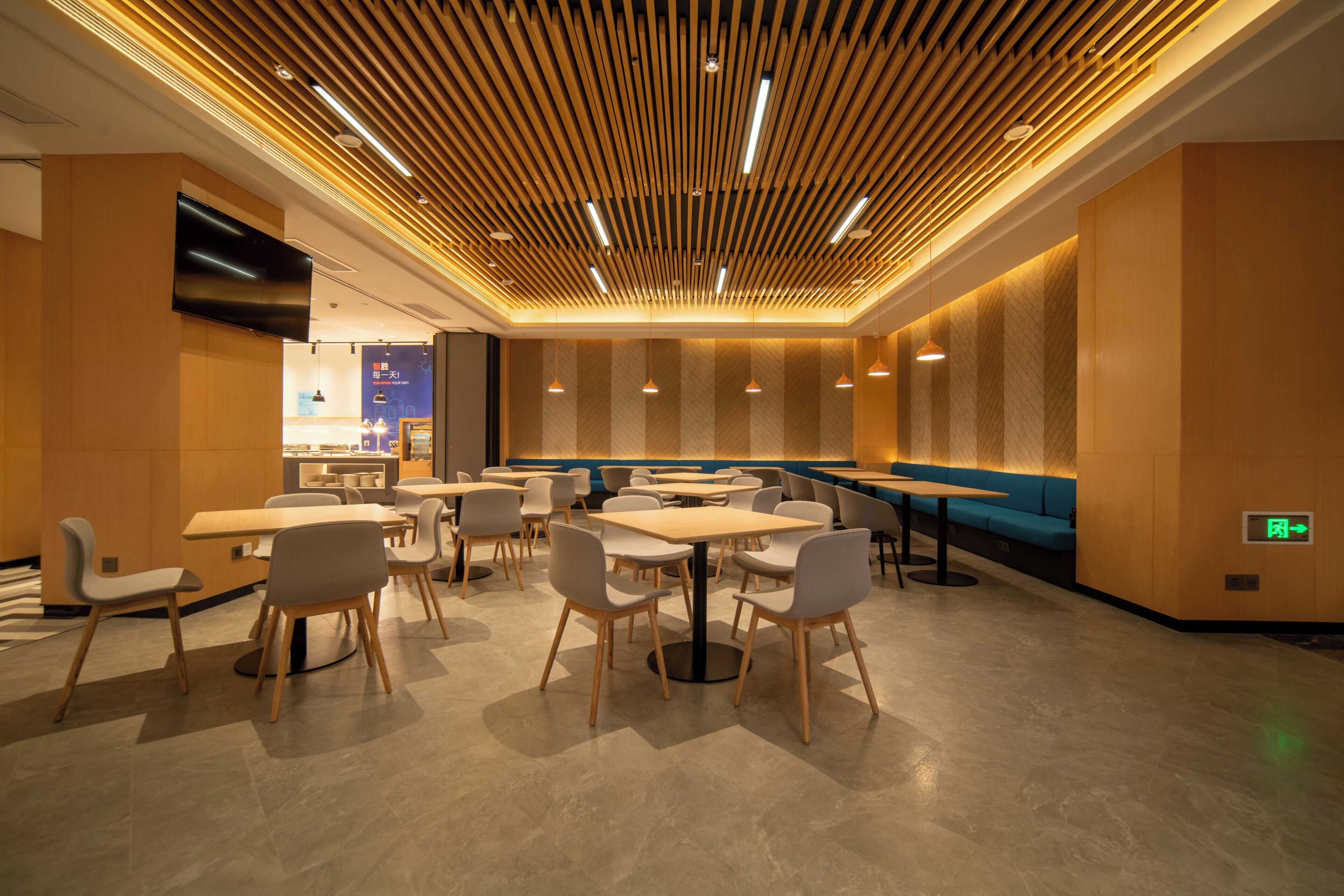 A modern restaurant interior with wooden panel ceilings, multiple dining tables and chairs, and a blue accent wall.