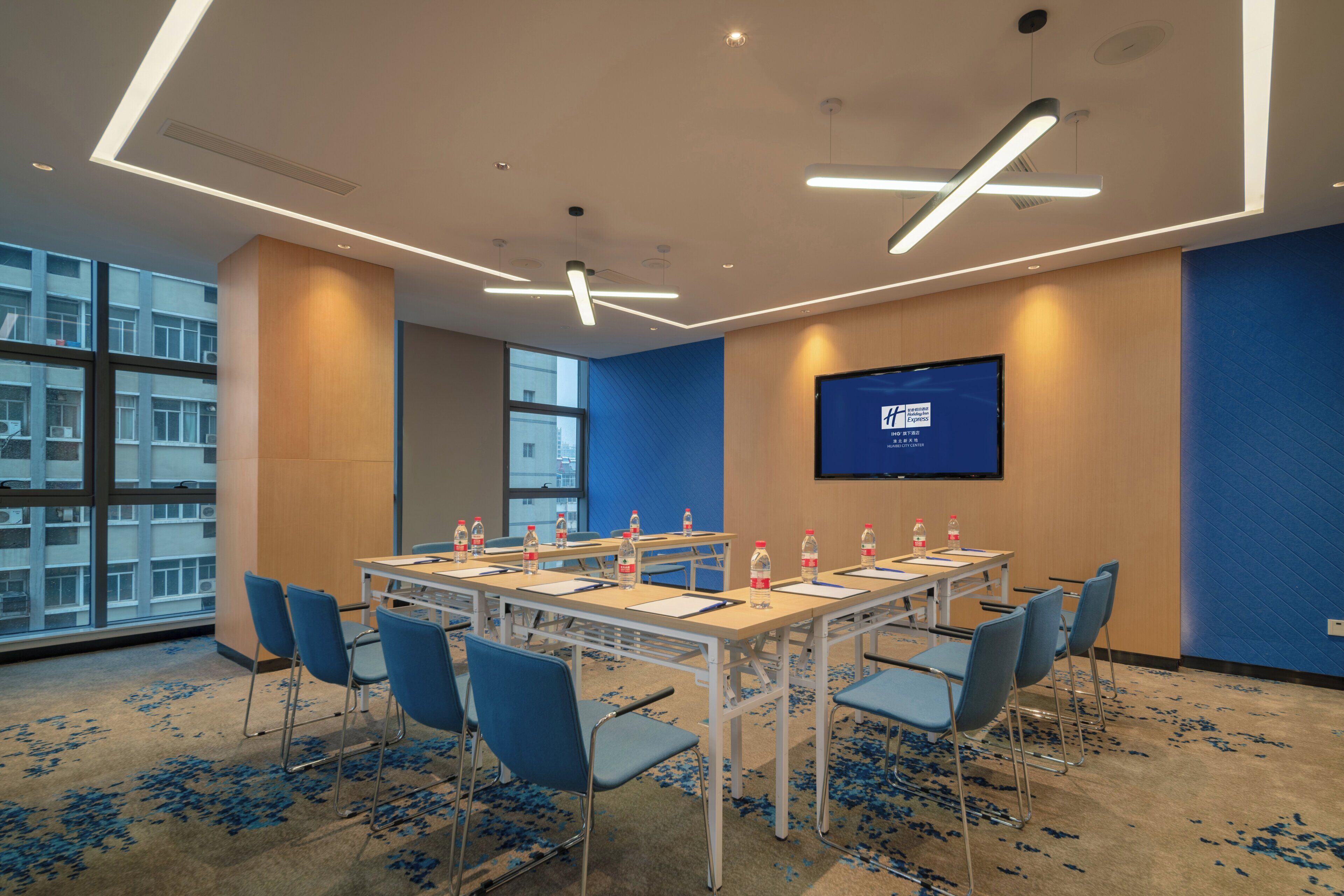 A conference room with a long table, blue chairs, and a screen on the wall.