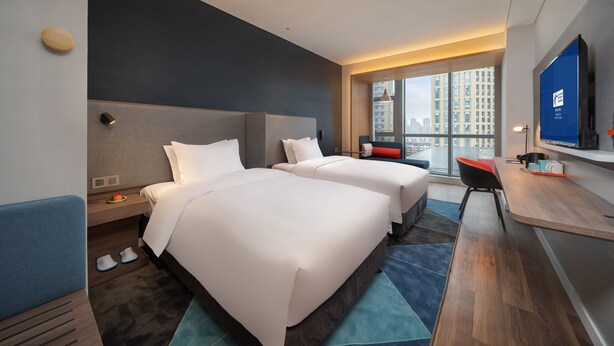 A hotel room with two beds, a desk, a TV, and a view of the city. - Holiday Inn Express Huaibei City Center by IHG (Huaibei)