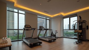 A modern gym with treadmills, a stationary bike, and weight machines, featuring large windows and a high ceiling. - Holiday Inn Express Huaibei City Center by IHG (Huaibei)