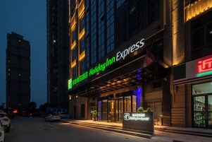 Entrada de un hotel con un letrero de Holiday Inn Express, puerta de cristal y un estacionamiento con coches.
