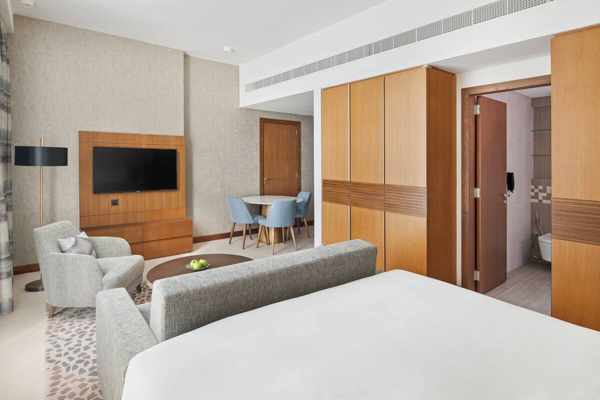 Une chambre d’hôtel moderne dotée d’un grand lit, d’un téléviseur à écran plat fixé au mur, d’un coin repas avec une table et des chaises, et d’une armoire avec des portes coulissantes.