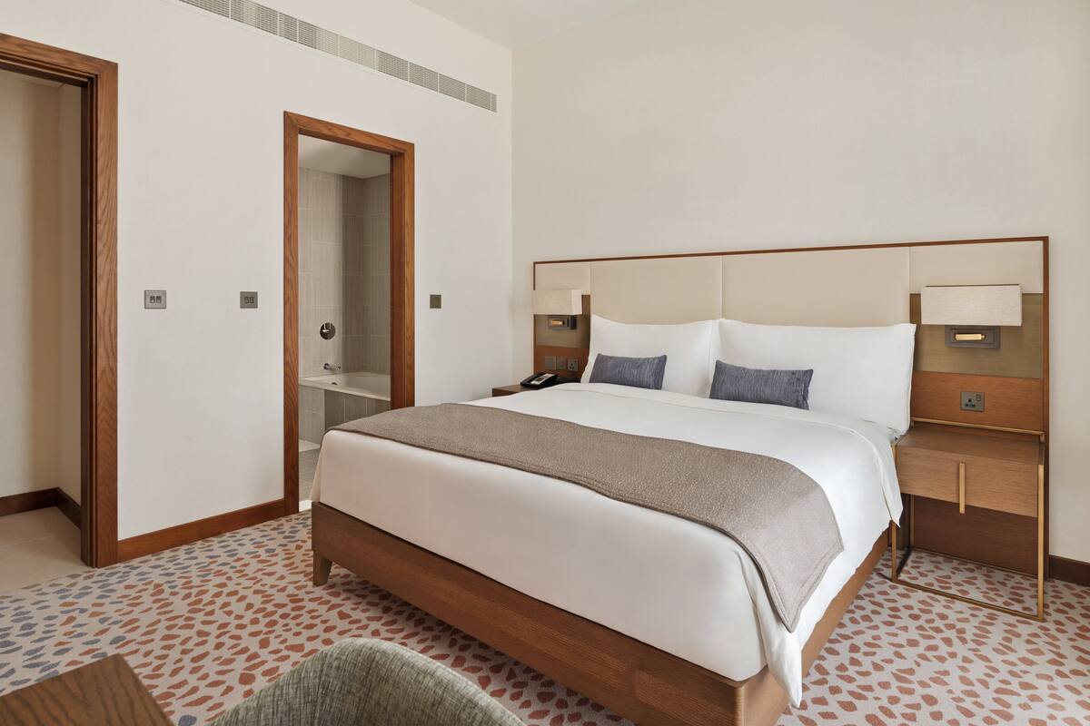 Une chambre d’hôtel avec un grand lit, des tables de chevet, un miroir et une porte.