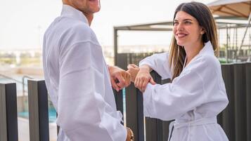 A couple in white robes standing by a poolside, holding hands.